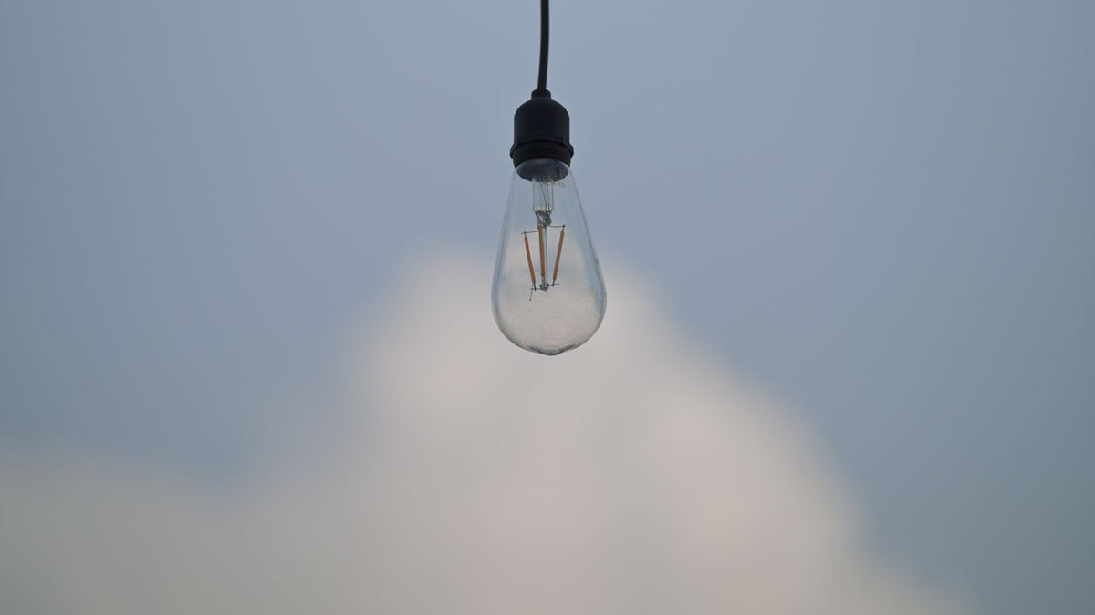 Ampoule suspendue contre un ciel bleu doux, symbole de la lumière