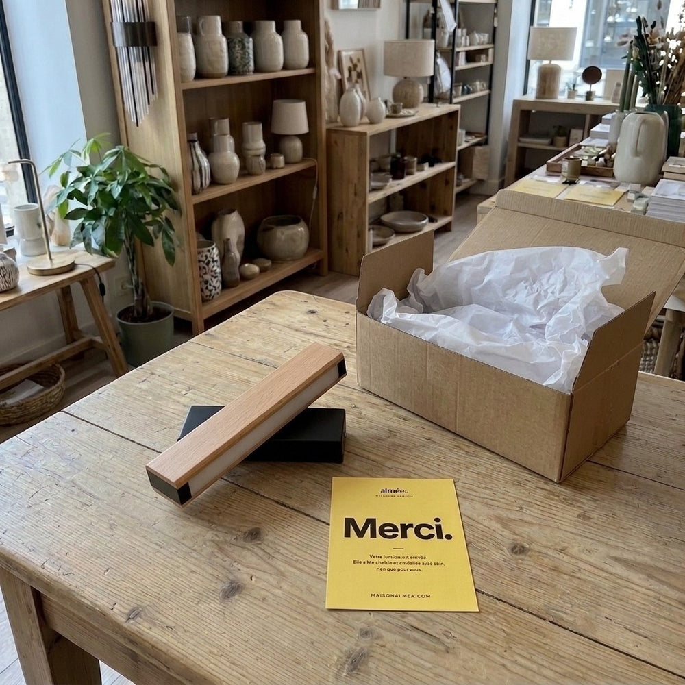 Liseuse pivotante en bois et métal noir posée sur une table de boutique, à côté de son carton et de la carte Merci #noir #21-cm
