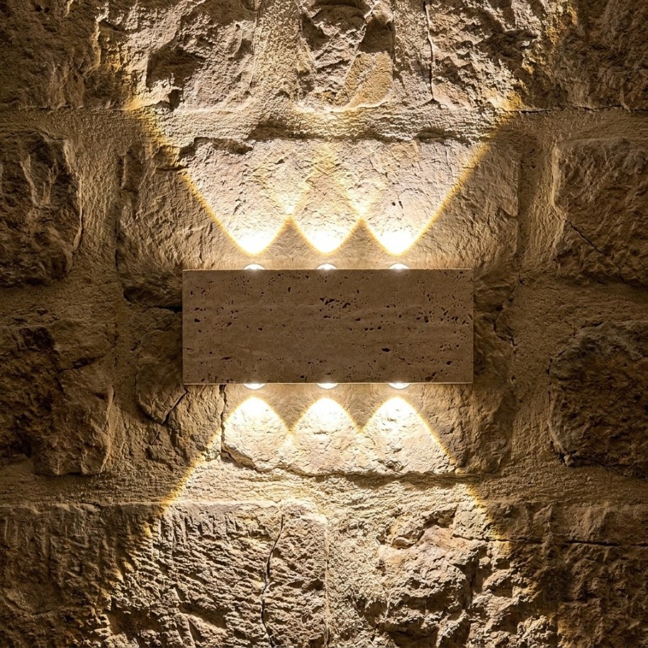 Applique en travertin allumée la nuit sur un vieux mur de pierres