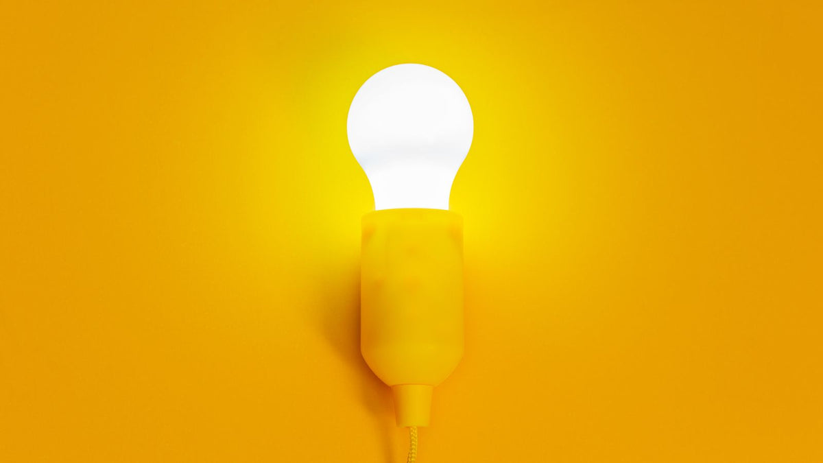 Ampoule allumée sur une douille murale devant un fond jaune