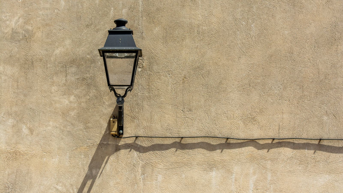 Applique lanterne en métal noir sur un mur beige texturé