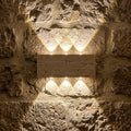 Applique en travertin allumée la nuit sur un vieux mur de pierres