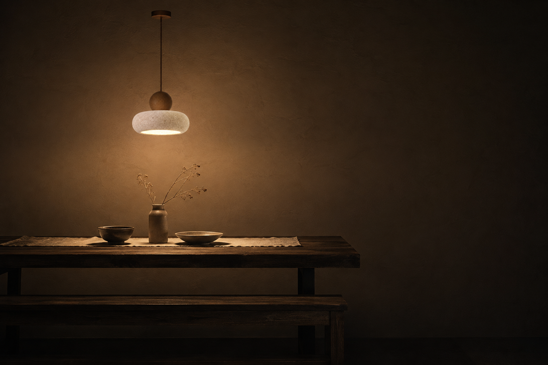Salle à manger dans le noir, la suspension en travertin est la seule source allumée et dessine un cercle de lumière sur la table