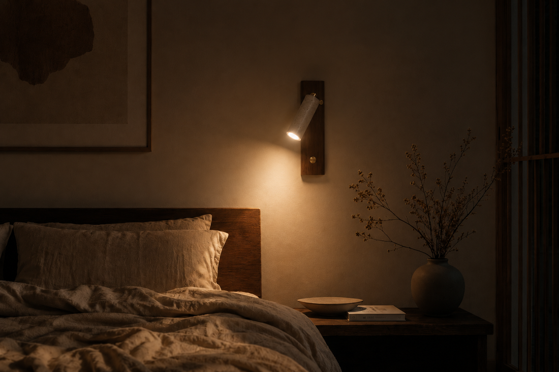 Chambre dans le noir, l'applique en travertin est la seule source allumée et pose un halo chaud sur le mur