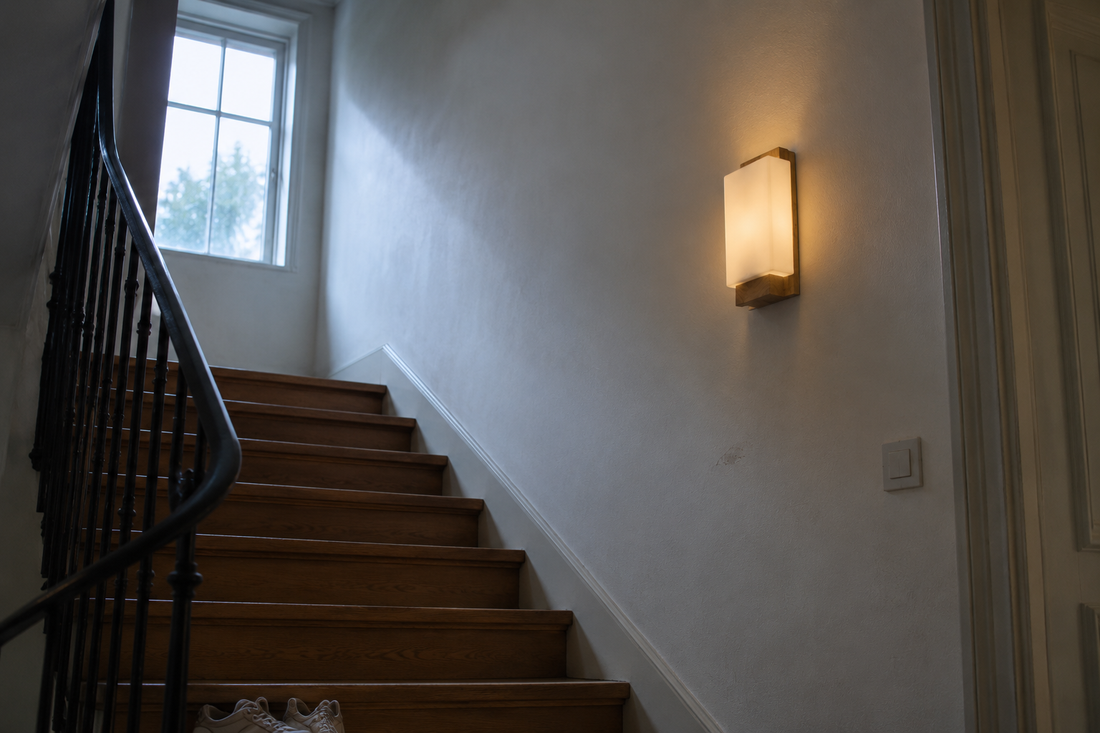 Applique en bois et verre allumée dans une montée d'escalier au petit matin