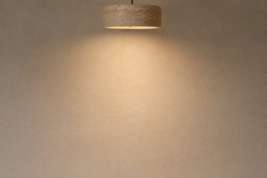 Mur à la chaux crème révélé par la lumière chaude et rasante de la suspension en travertin
